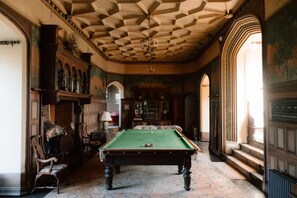 A billiards room with a pool table, wooden chairs, and a decorative ceiling.