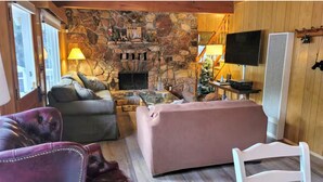 Een gezellig interieur van een chalet met een stenen openhaard, leren banken, een televisie en een houten wand.