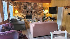 Ein gemütliches Blockhaus-Interieur mit Kamin aus Stein, Ledersofas, einem Fernseher und einer Holzwand.