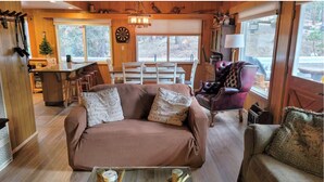 Een gezellig interieur van een chalet met een bank, fauteuils, een eettafel en een barhoek.