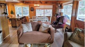 Ein gemütliches Blockhaus-Interieur mit einer Couch, Sesseln, einem Esstisch und einer Bar.