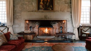 A stone fireplace with a fire, a red sofa, and a painting above the fireplace. - Lovingly restored castle in the Scottish Borders (Oxnam)