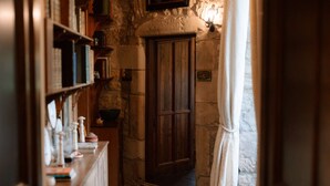 A narrow hallway with a wooden door, stone walls, and shelves with various items. - Lovingly restored castle in the Scottish Borders (Oxnam)