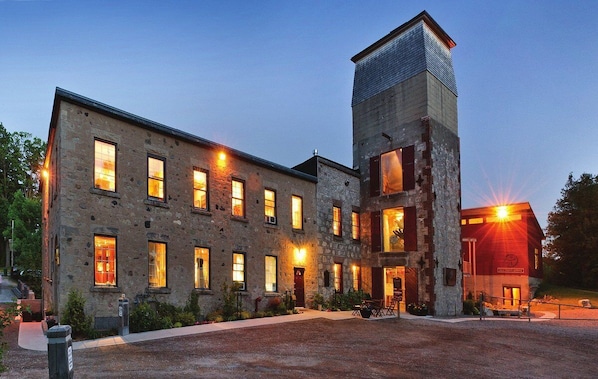 A stone building with multiple windows and a central tower, surrounded by a gravel driveway and greenery.