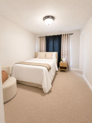 A bedroom with a bed, a bedside table, a lamp, and a window with curtains.