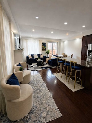 Una sala moderna con un sofá, sillas, una mesa de centro y una zona de cocina con barra.
