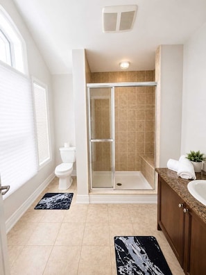 A bathroom with a glass-enclosed shower, a toilet, a sink, and a potted plant.