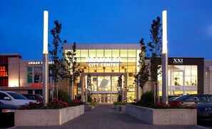 A modern building with a glass facade, labeled 'BRAMAIA CITY CENTRE,' surrounded by parked cars and featuring prominent signage for 'URBAN VET' and 'XXI FOREVER.' - Cozy 3BR Caledon Retreat with Patio & Outdoor BBQ (Caledon)