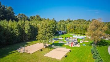 A park with a playground, a tennis court, and a building in the background.
