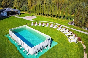 A rectangular swimming pool with a surrounding deck, surrounded by a well-manicured lawn and a row of white lounge chairs. - Comfortable Holiday Home no. 2B With a Fireplace (Darlowo)