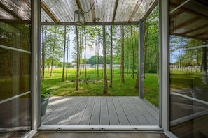 Ein Zimmer mit Glaswand, Holzterrasse und Blick auf Wald und See.