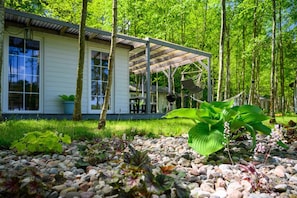 Ein Haus mit Veranda, umgeben von einem Garten mit verschiedenen Pflanzen und einem Kiesweg.