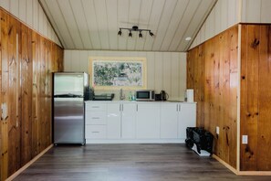 A kitchen with wooden walls, a stainless steel refrigerator, a microwave, and a sink. - 3-Bedroom Cottage #9 (Nobel)