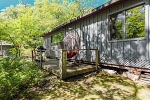 A wooden cabin with a porch, a grill, and a large decorative item. - 3-Bedroom Cottage #9 (Nobel)
