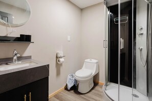 A bathroom with a sink, toilet, and glass-enclosed shower. - 3-Bedroom Cottage #9 (Nobel)