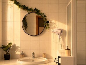 Ein Badezimmer mit rundem Spiegel, einem Fön, einem Waschbecken und einer Topfpflanze.