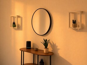 Ein Zimmer mit einem runden Spiegel, zwei Wandpflanzgefäßen, einem kleinen Tisch mit einem Lautsprecher und einer Topfpflanze.