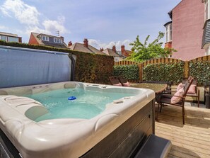A hot tub in a backyard with a wooden deck, chairs, and a hedge. - Tapestry House (Bridlington)