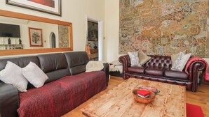 Un salon avec un canapé en cuir foncé, une table basse en bois et une tapisserie à motifs accrochée au mur.
