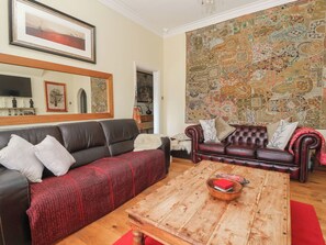 A living room with a dark leather sofa, a wooden coffee table, and a patterned tapestry on the wall. - Tapestry House (Bridlington)