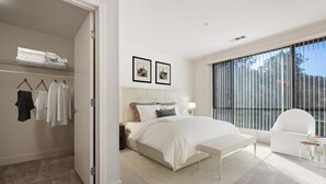 Un dormitorio moderno con una cama grande, una mesita de noche, una silla y un armario.