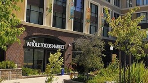 Edificio de Whole Foods Market con fachada de ladrillo, ventanas amplias y una zona ajardinada con árboles y arbustos.