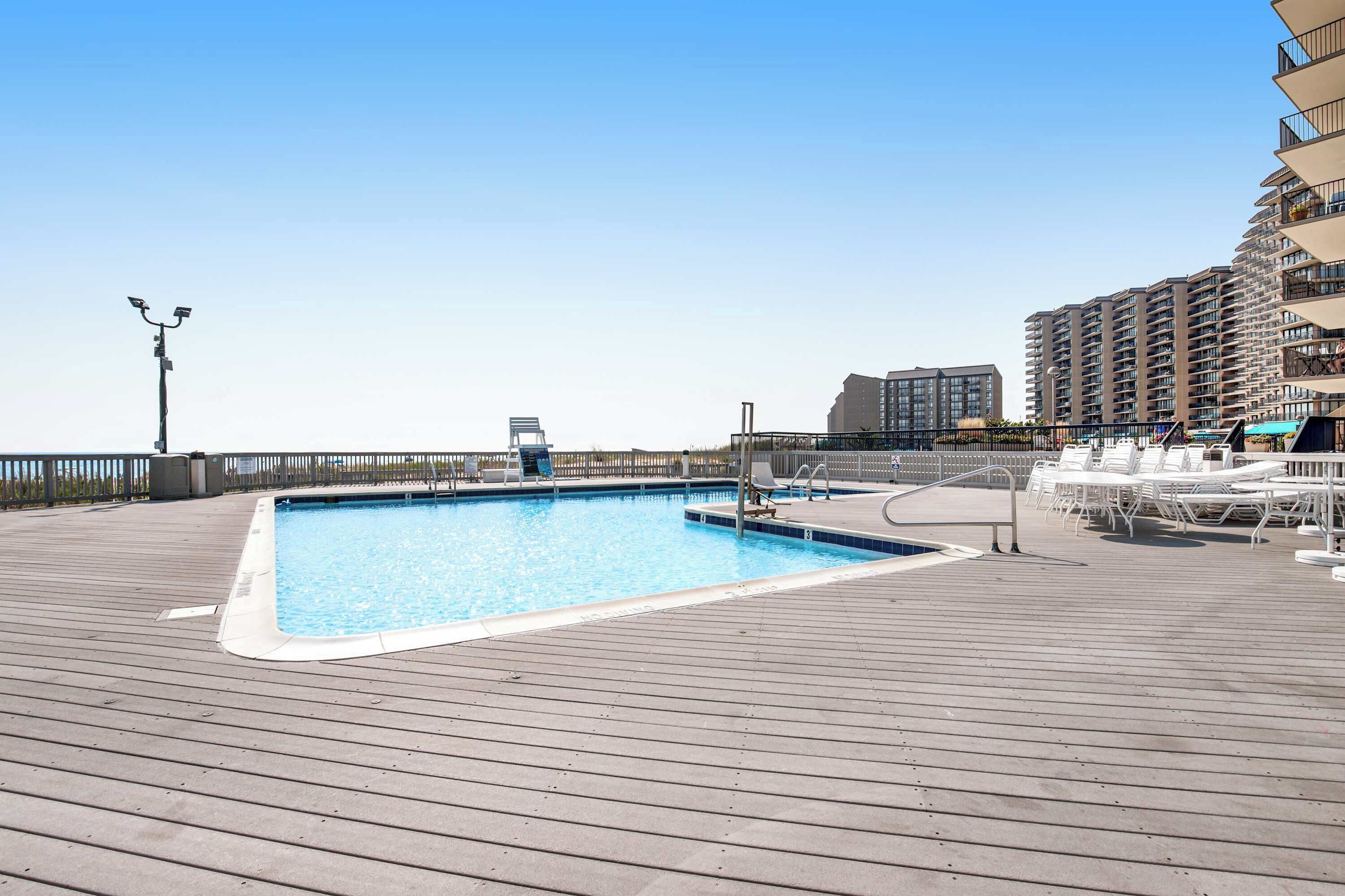 Una piscina su un pontile di legno con lettini e una ringhiera.