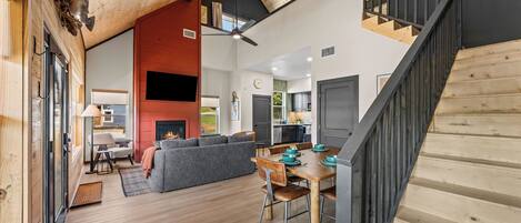 A spacious living area with a fireplace, a dining table, and a staircase.