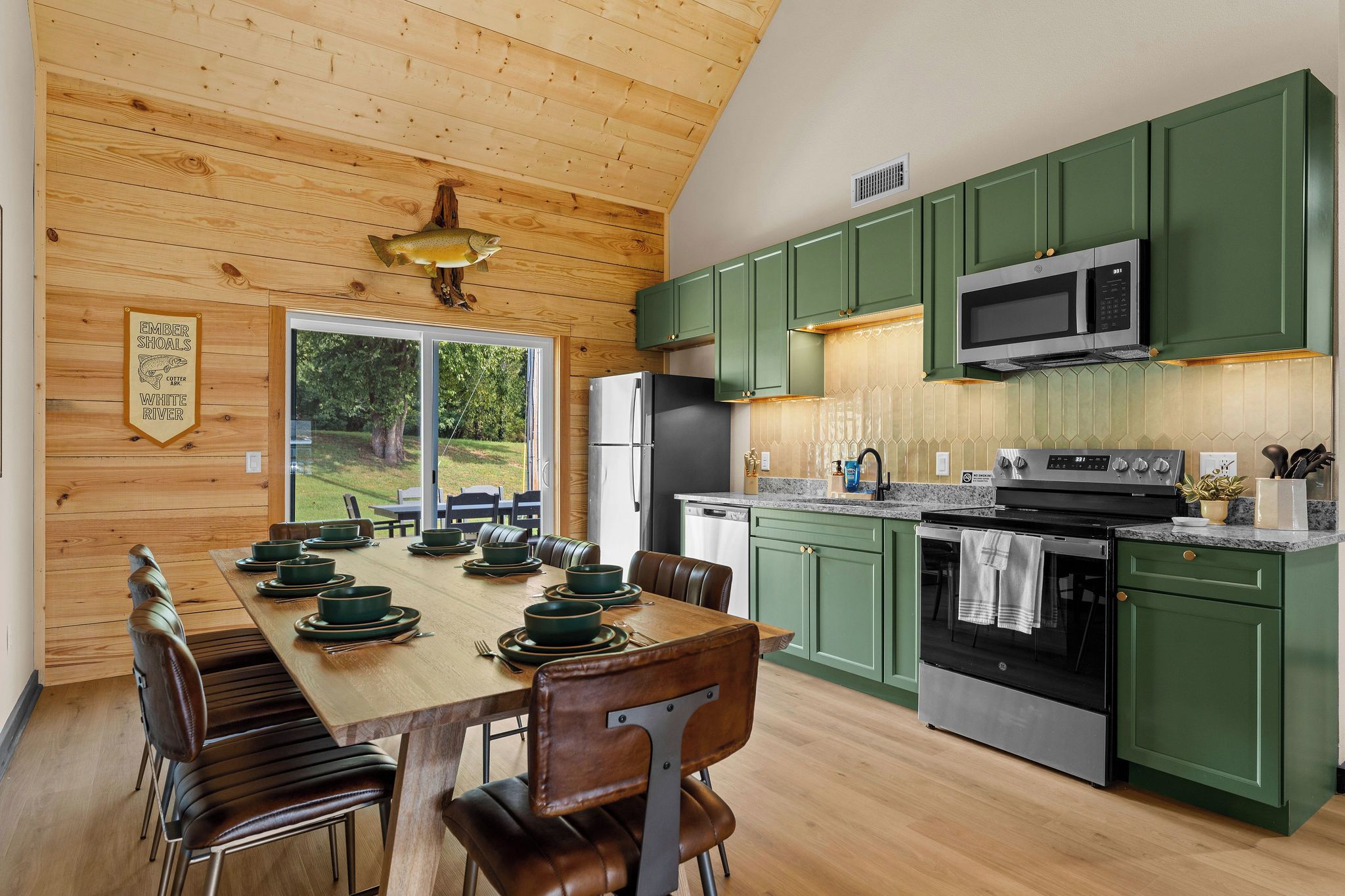 A modern kitchen with green cabinets, stainless steel appliances, and a dining area with a wooden table and leather chairs.