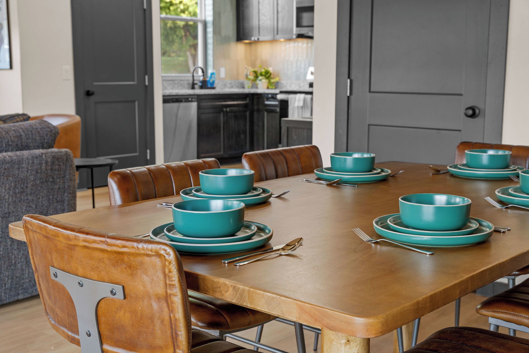 A dining table set with teal bowls and plates, surrounded by leather chairs.
