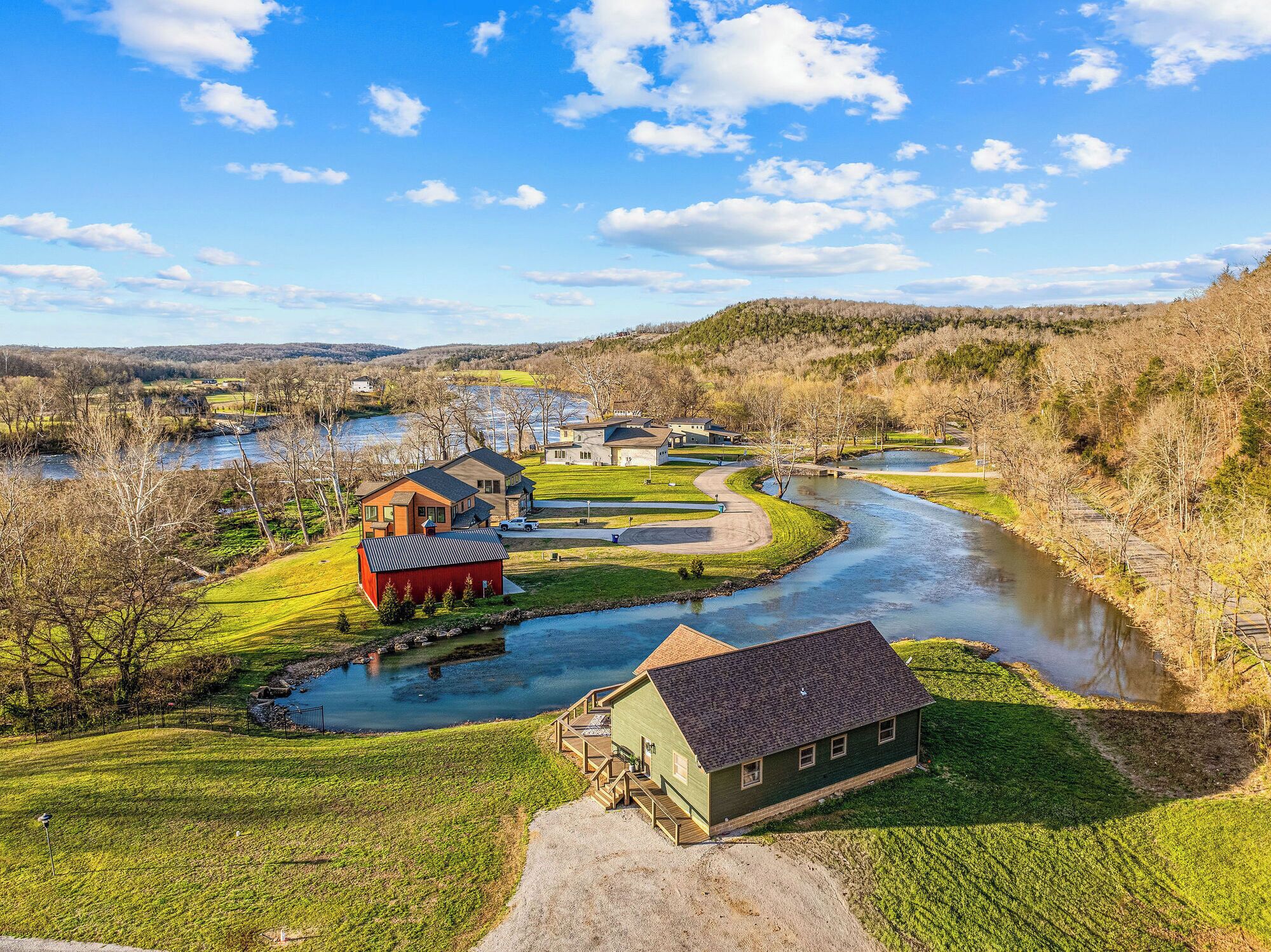 A riverside property with a house, a red barn, and a green building with a deck.