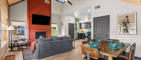 A spacious living area with a fireplace, a dining table set for four, and a kitchen in the background.