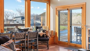 A room with a wooden ceiling, large windows, a dining area with chairs and a table, and a sliding glass door leading outside.
