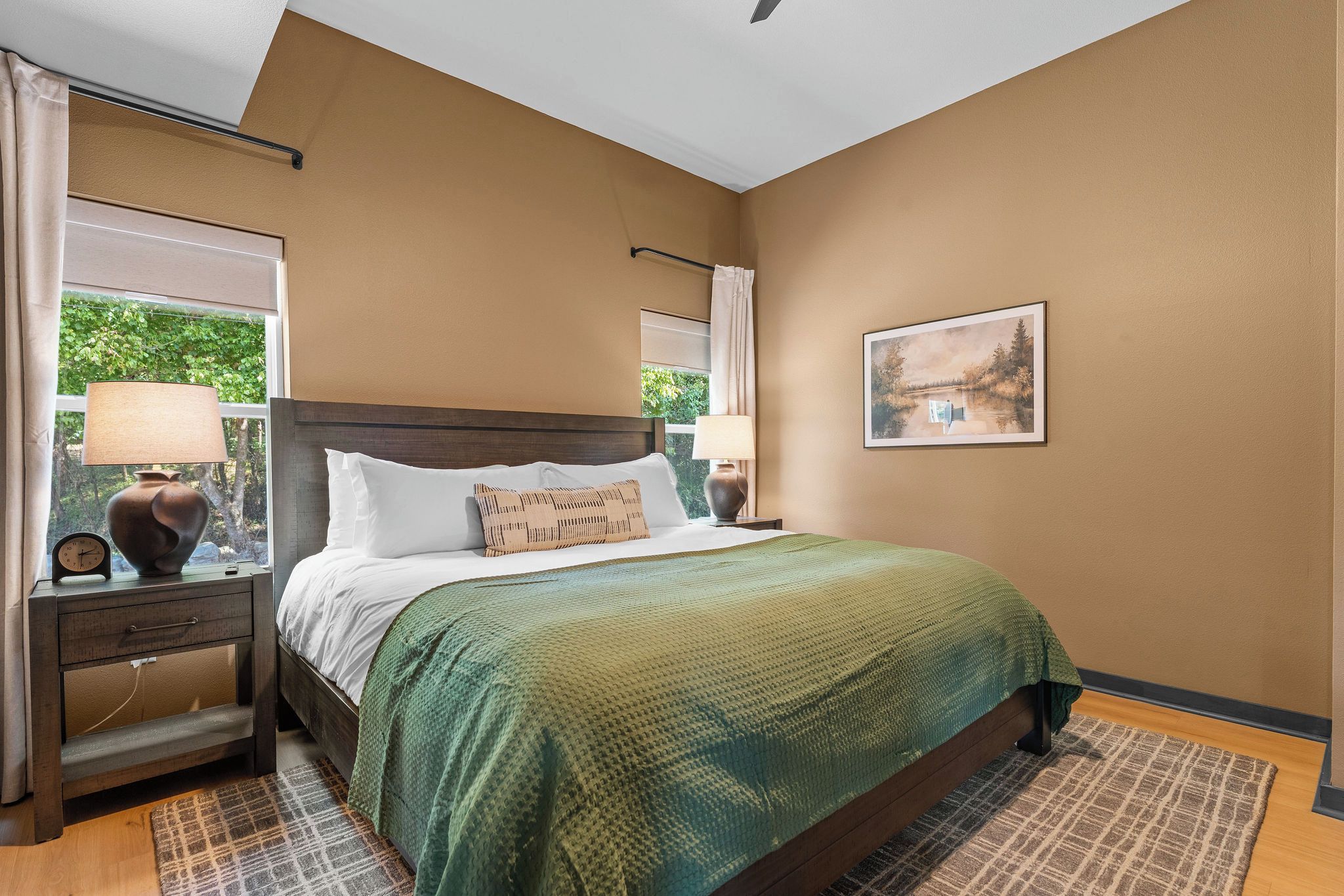 Quarto com cama, mesas de cabeceira, abajur, relógio e um quadro na parede.
