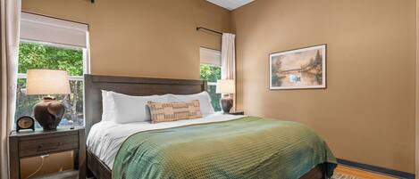 Quarto com cama, mesas de cabeceira, abajur, relógio e um quadro na parede.