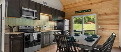 A modern kitchen with dark cabinetry, stainless steel appliances, and a dining area with a table set for four.