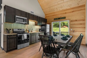A modern kitchen with dark cabinetry, stainless steel appliances, and a dining area with a table set for four. -  Ember Shoals Resort | On the White River, Cotter AR (Cotter)