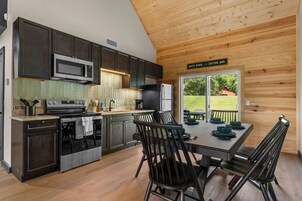 Una cocina moderna con muebles oscuros, electrodomésticos de acero inoxidable y un comedor con una mesa preparada para cuatro.