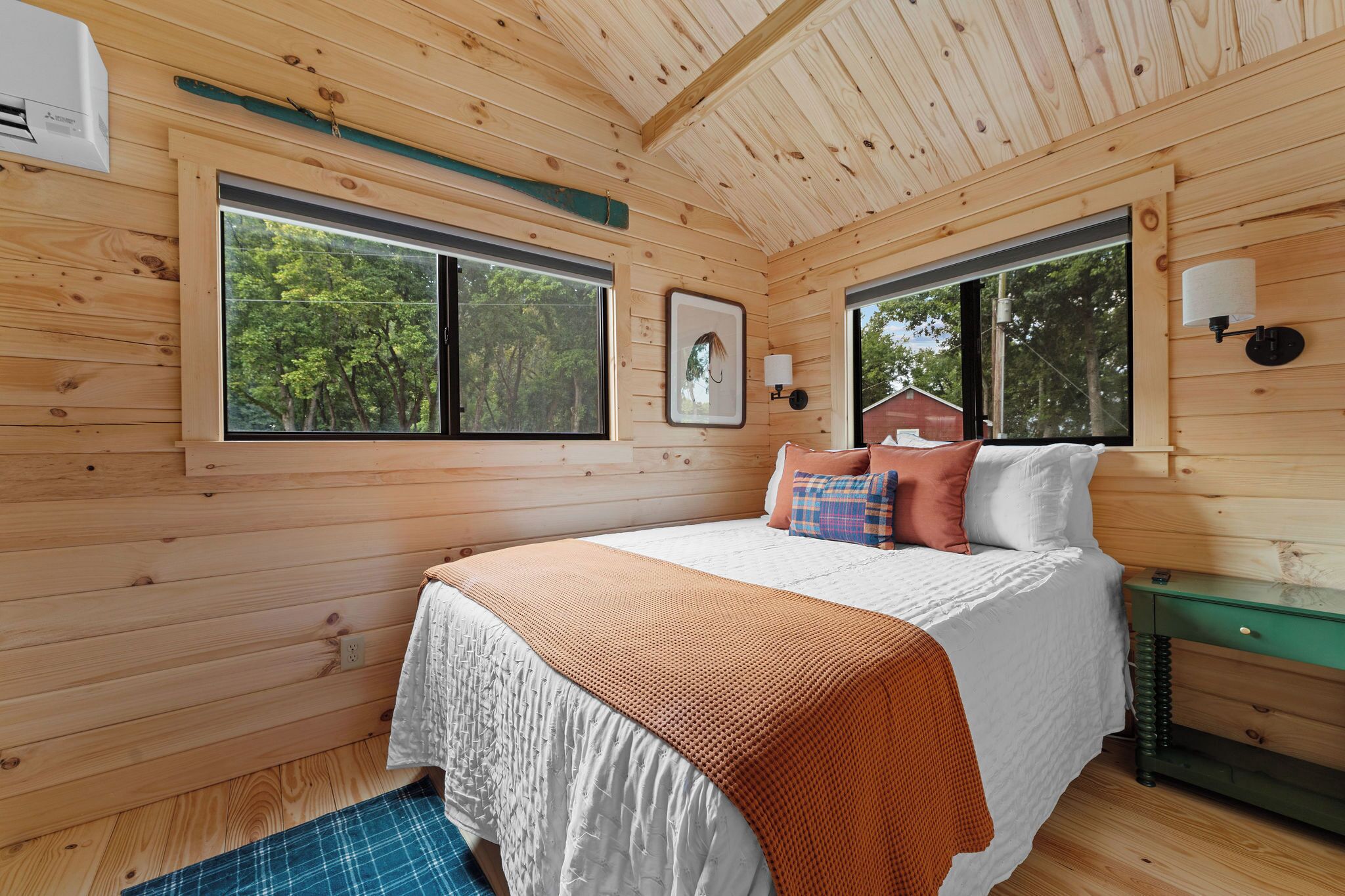 A wooden cabin bedroom with a bed, pillows, a nightstand, and a window.