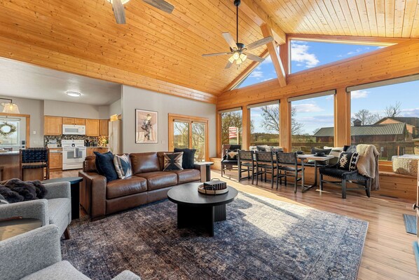 A spacious living room with a large wooden ceiling, a dining area with outdoor seating, and a kitchen with wooden cabinets. -  Ember Shoals Resort | On the White River, Cotter AR (Cotter)