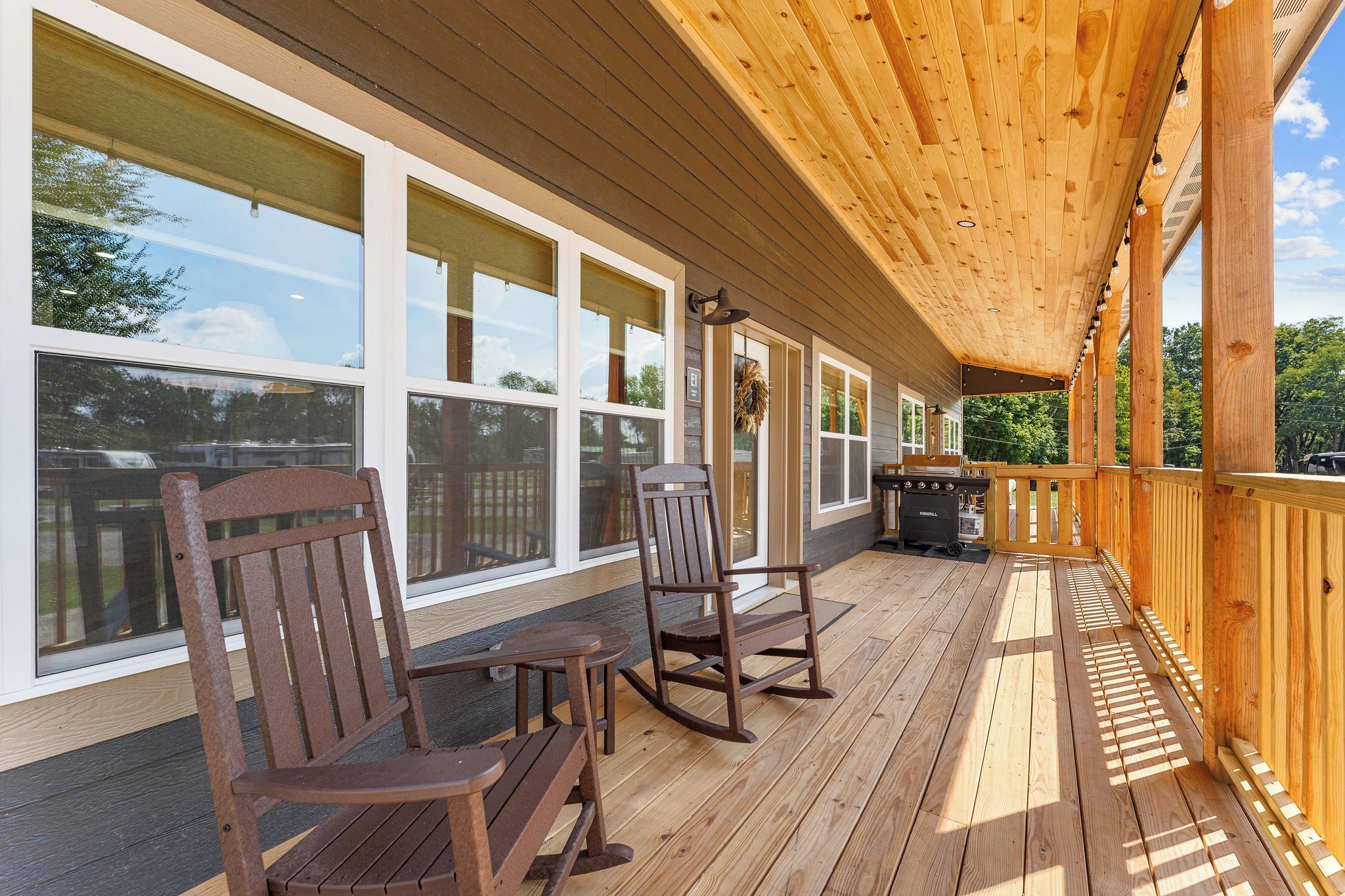 Un espace extérieur abrité avec un plancher en bois, deux fauteuils à bascule et un barbecue.