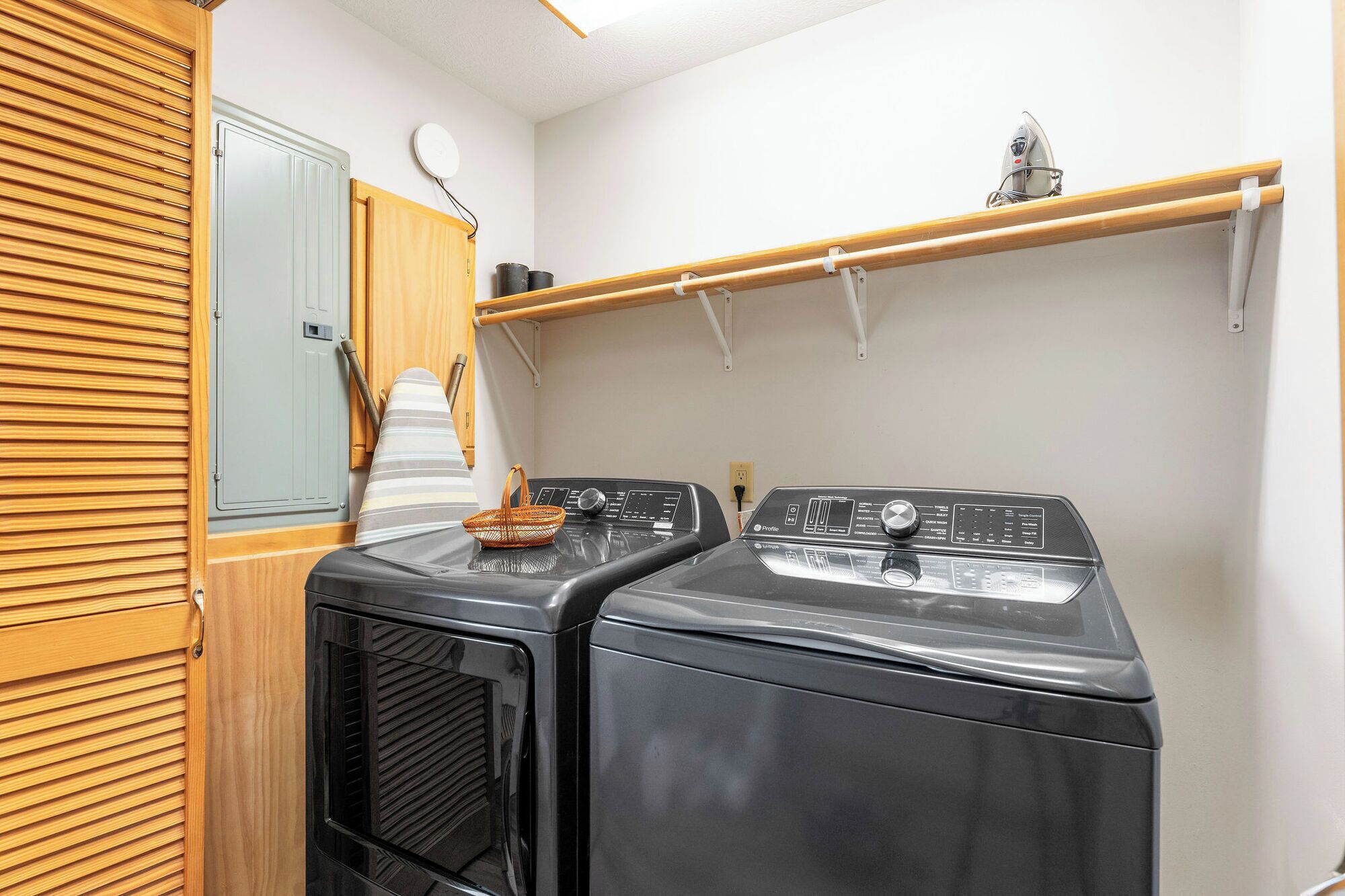 A laundry room with two front-loading washers, a wooden shelf, a mirror, and a hanging rack.