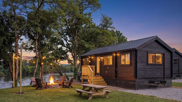 A cabin with a deck, a fire pit, and picnic tables.