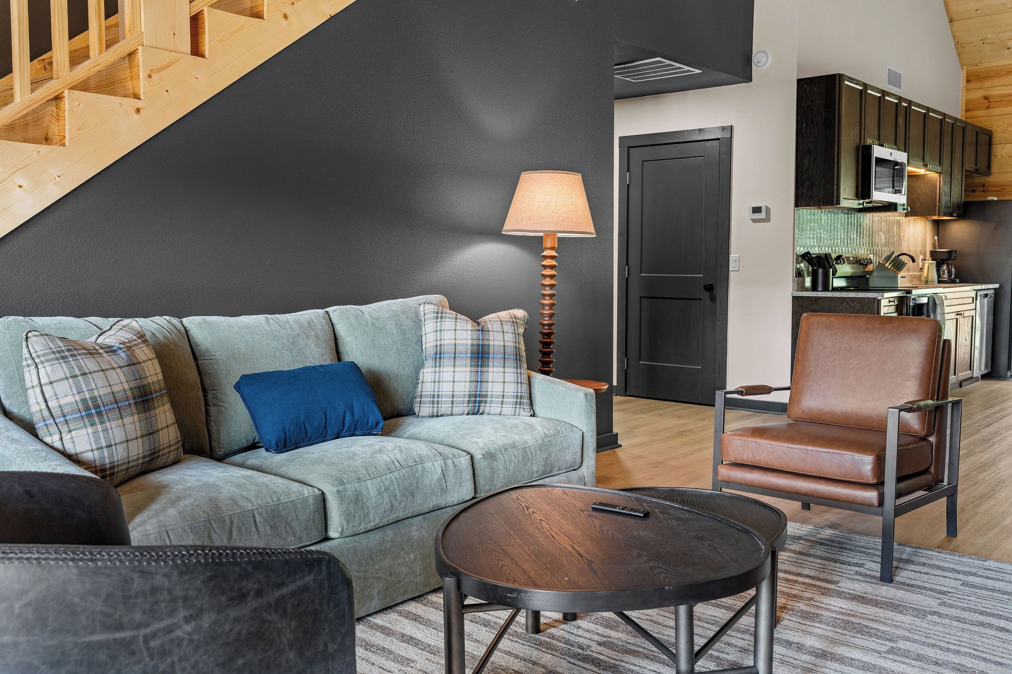 Una sala de estar moderna con sofá, sillón y mesa de centro, una escalera y una zona de cocina.