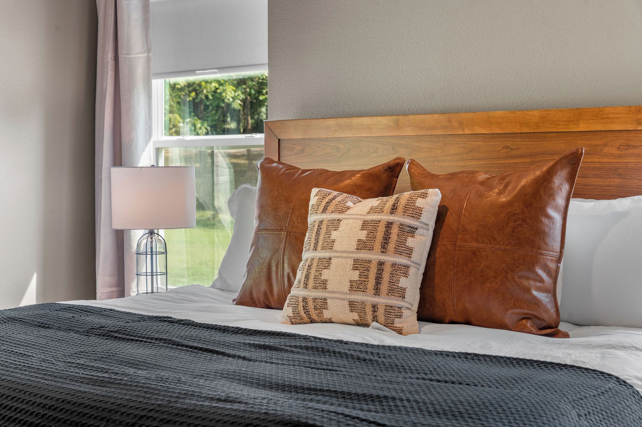 A bed with a wooden headboard, two brown pillows, a patterned pillow, and a dark gray blanket.