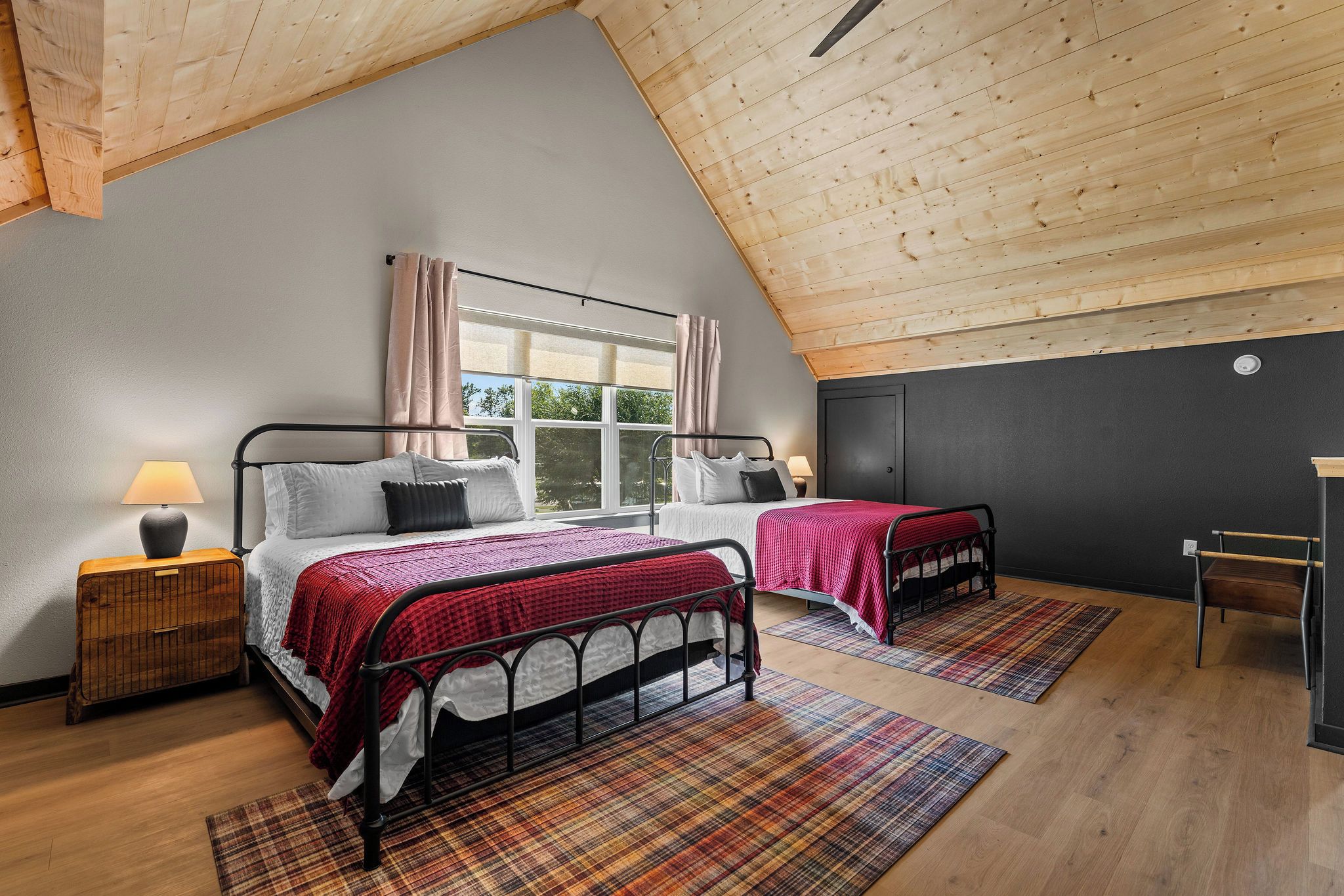 Un dormitorio con dos camas, una ventana con cortinas, una mesita de noche con lámpara y una silla.