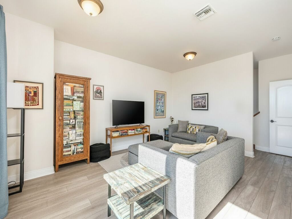Ein Wohnzimmer mit grauem Sofa, einem Flachbildfernseher, einem Bücherregal und einer Tür.