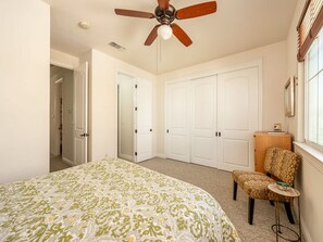 A bedroom with a bed, a chair, a ceiling fan, and white closets. - Modern Coastal Stay w/ Rooftop + Beach Gear (Oceanside)