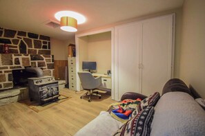 A room with a stone wall, a fireplace, a desk with a computer, a chair, and a couch. - Spa & Nature | La Halte (Marsoui)
