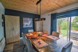 A wooden dining table with placemats, chairs, and a hanging light fixture.
